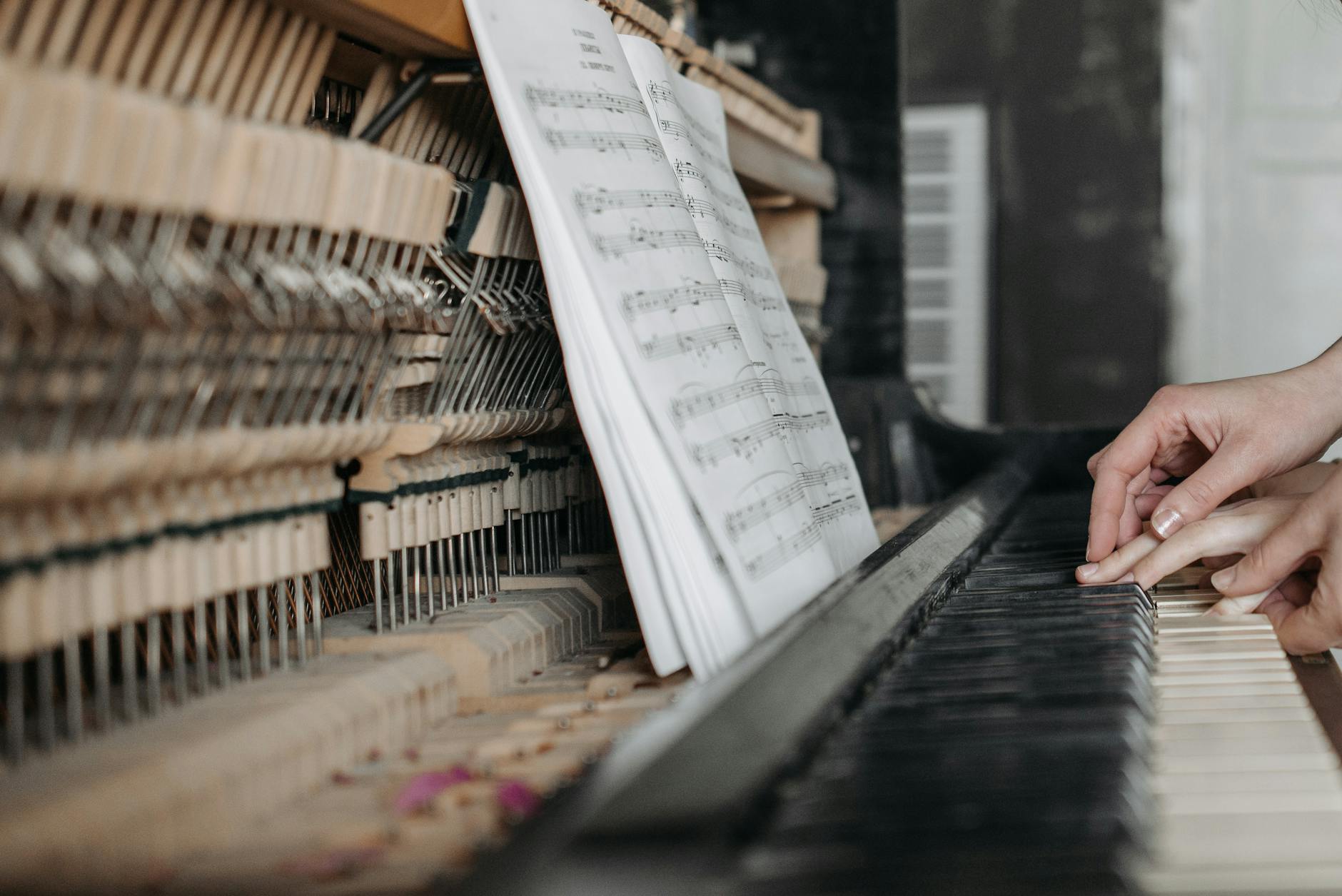 Close-up of hands playing piano keys with open sheet music, emphasizing learning and teaching.
