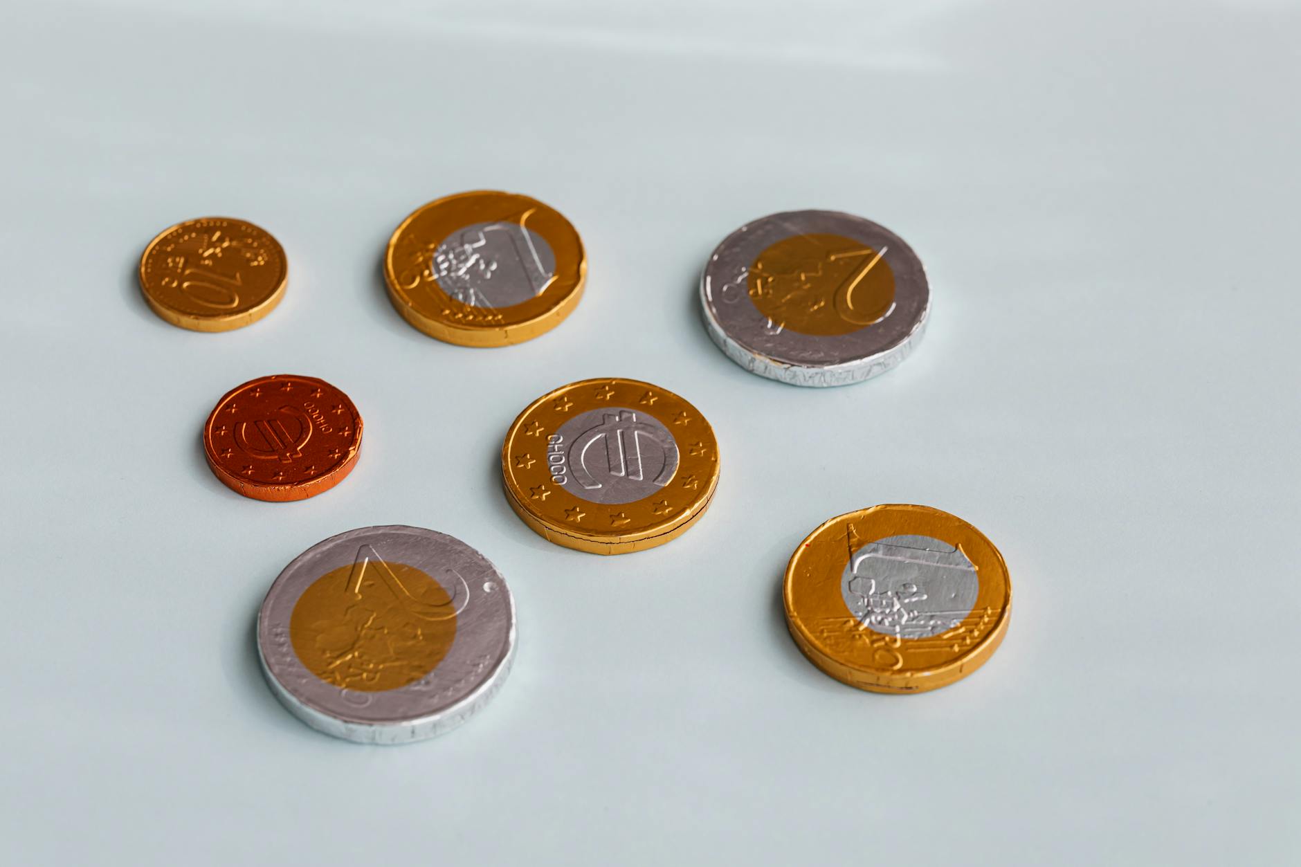 Chocolate coins resembling Euro currency scattered on a white surface, shot from above.