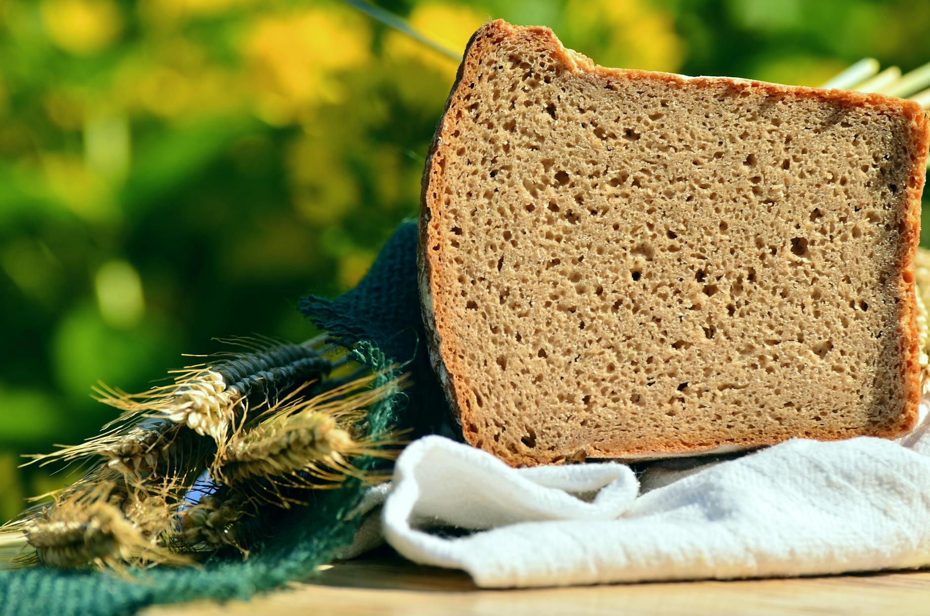 Close-up of rustic rye bread slice with wheat stalks on a sunny day.