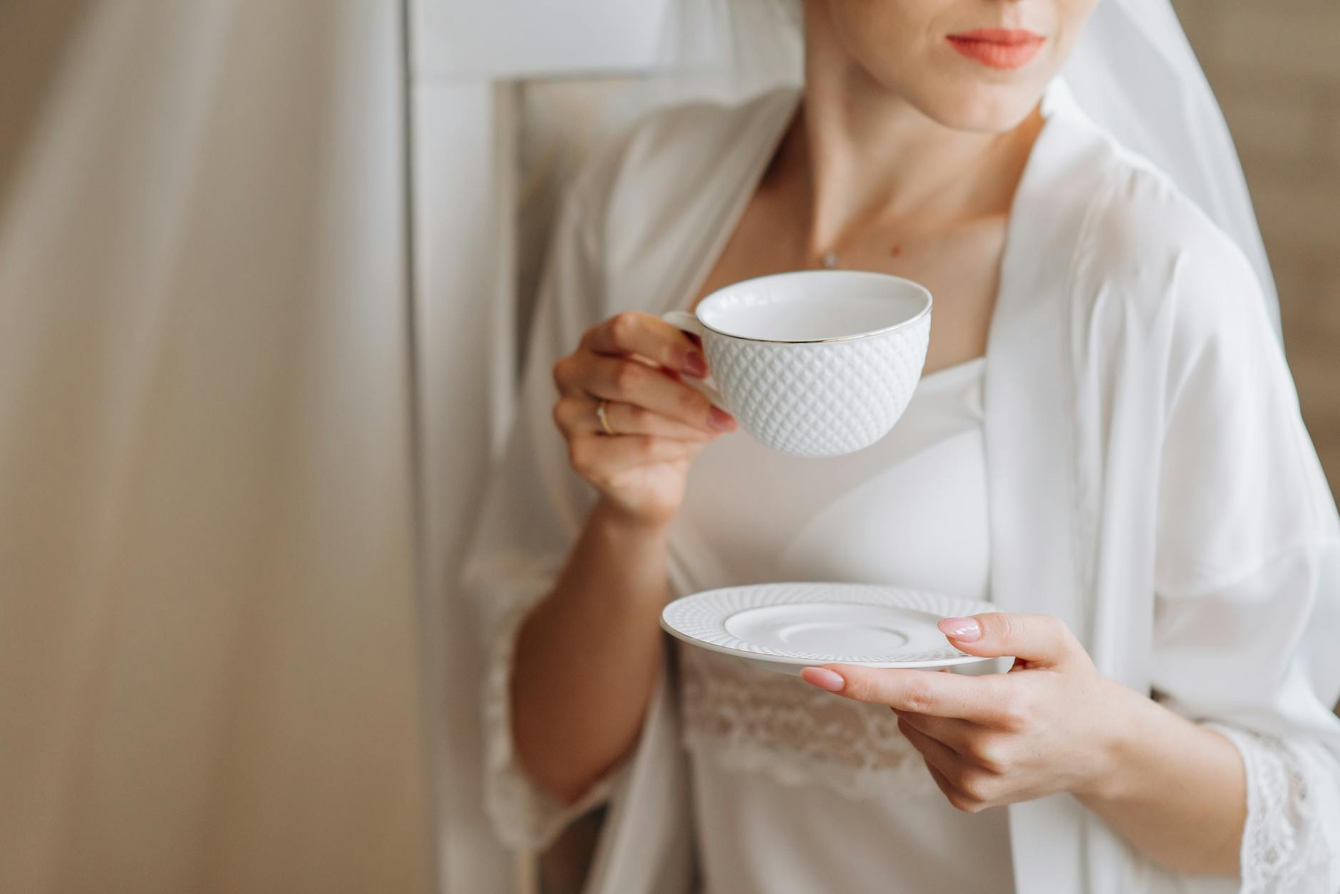 Close-up of a woman in a white robe sipping coffee indoors, exuding elegance and tranquility.