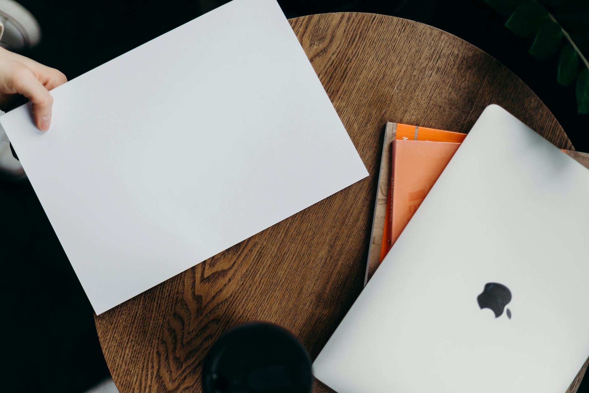 A top-down view of a minimalist workspace featuring a laptop and blank paper on a wooden table.