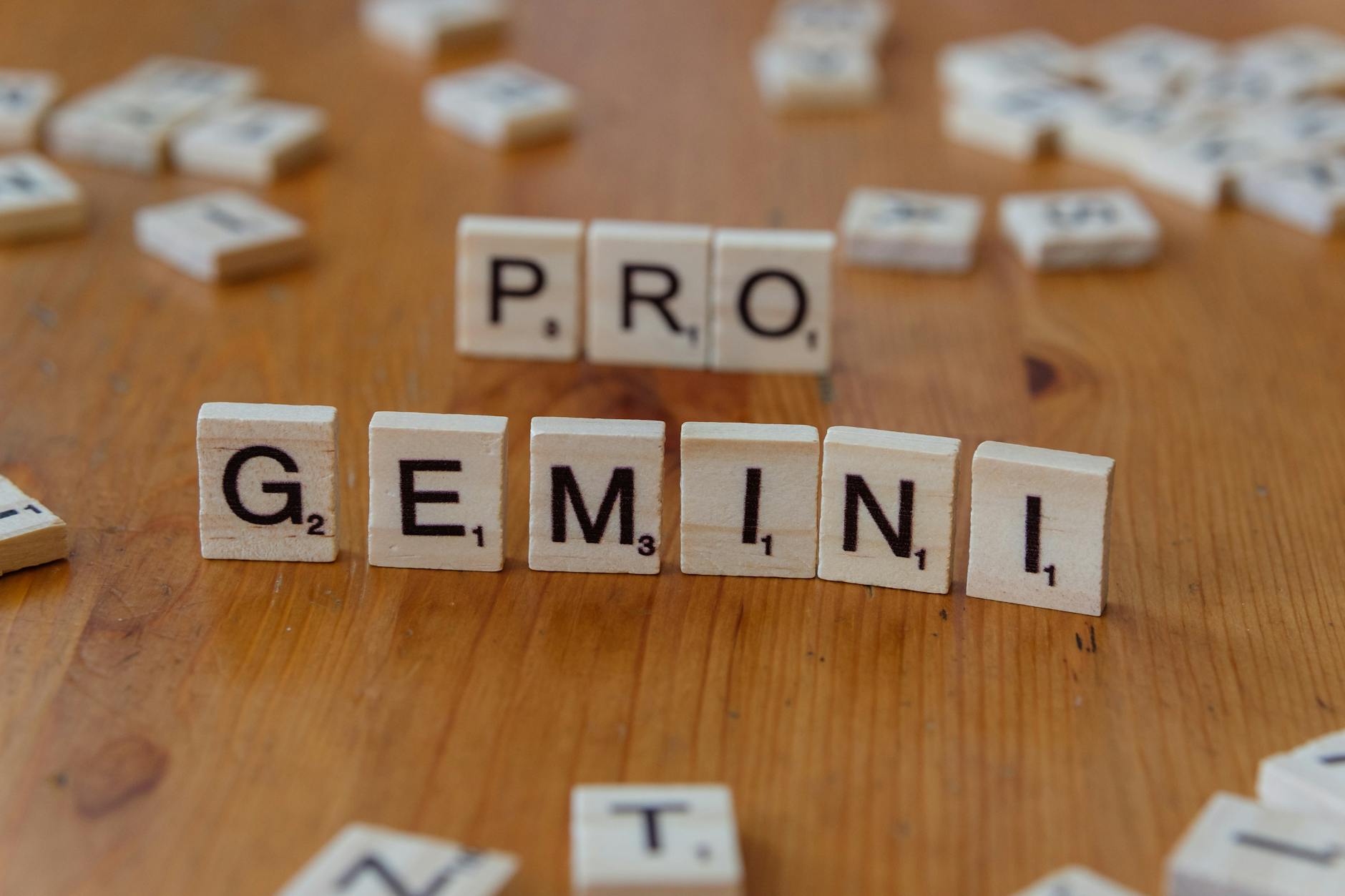 Scrabble tiles arranged to spell 'PRO GEMINI' on a wooden table, ideal for creativity themes.