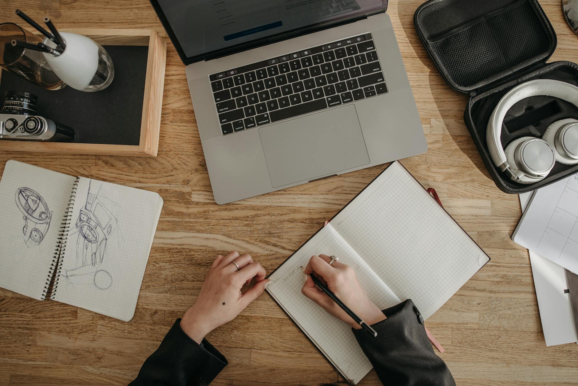Top view of a creative workspace featuring a laptop, sketchbooks, and headphones on a wooden desk.