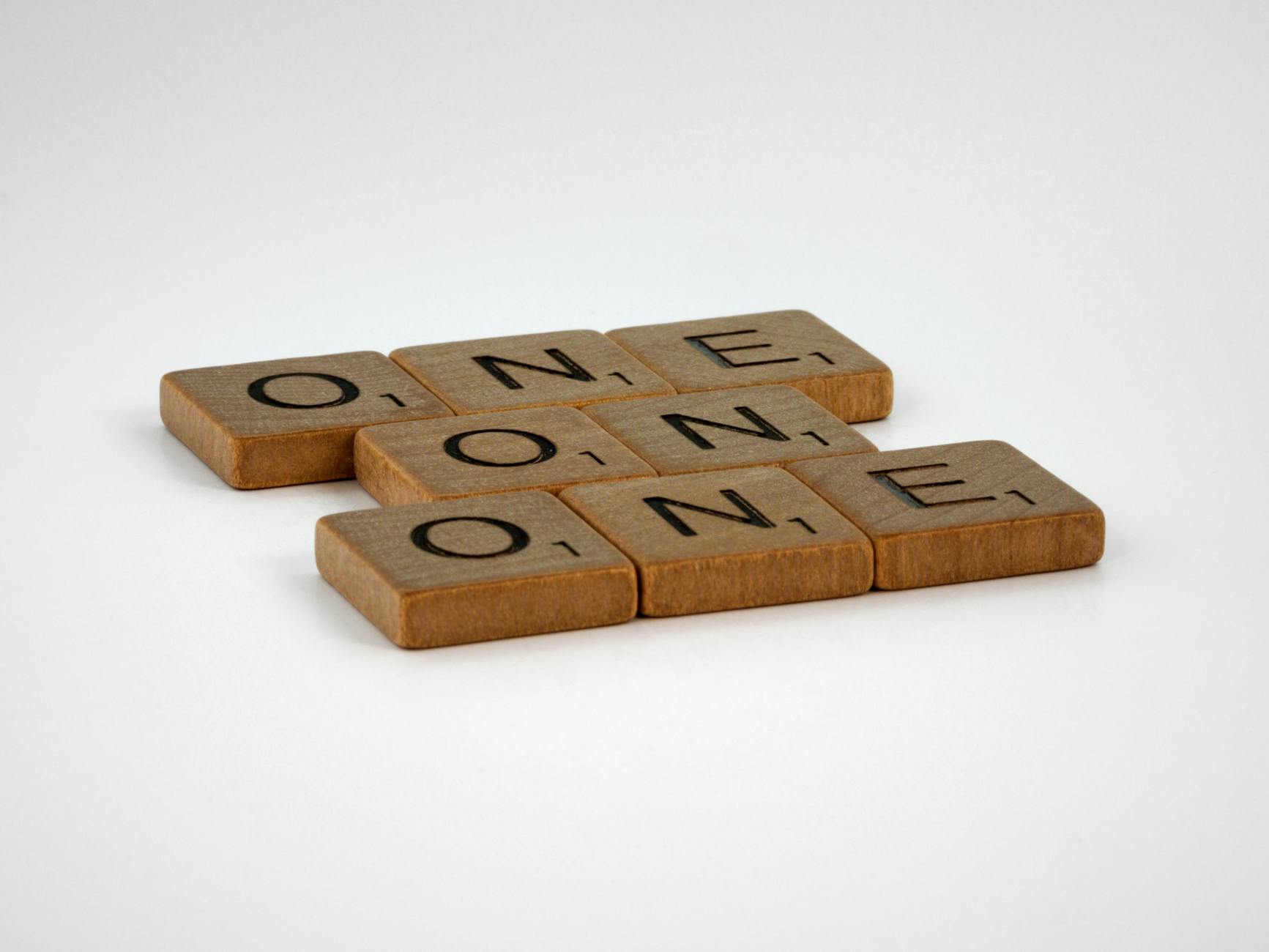 Scrabble tiles spelling 'ONE' arranged in an overlapping pattern on a plain background.